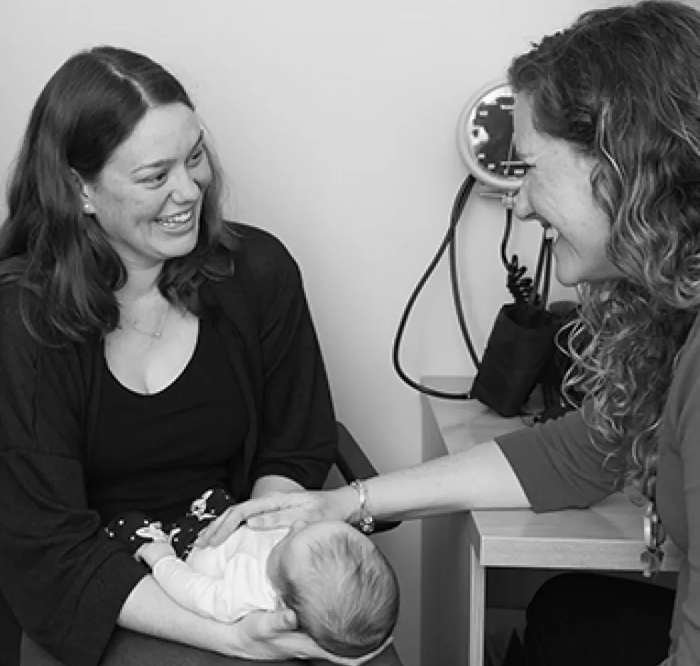 A clinician examining a newborn held by a parent during a baby check