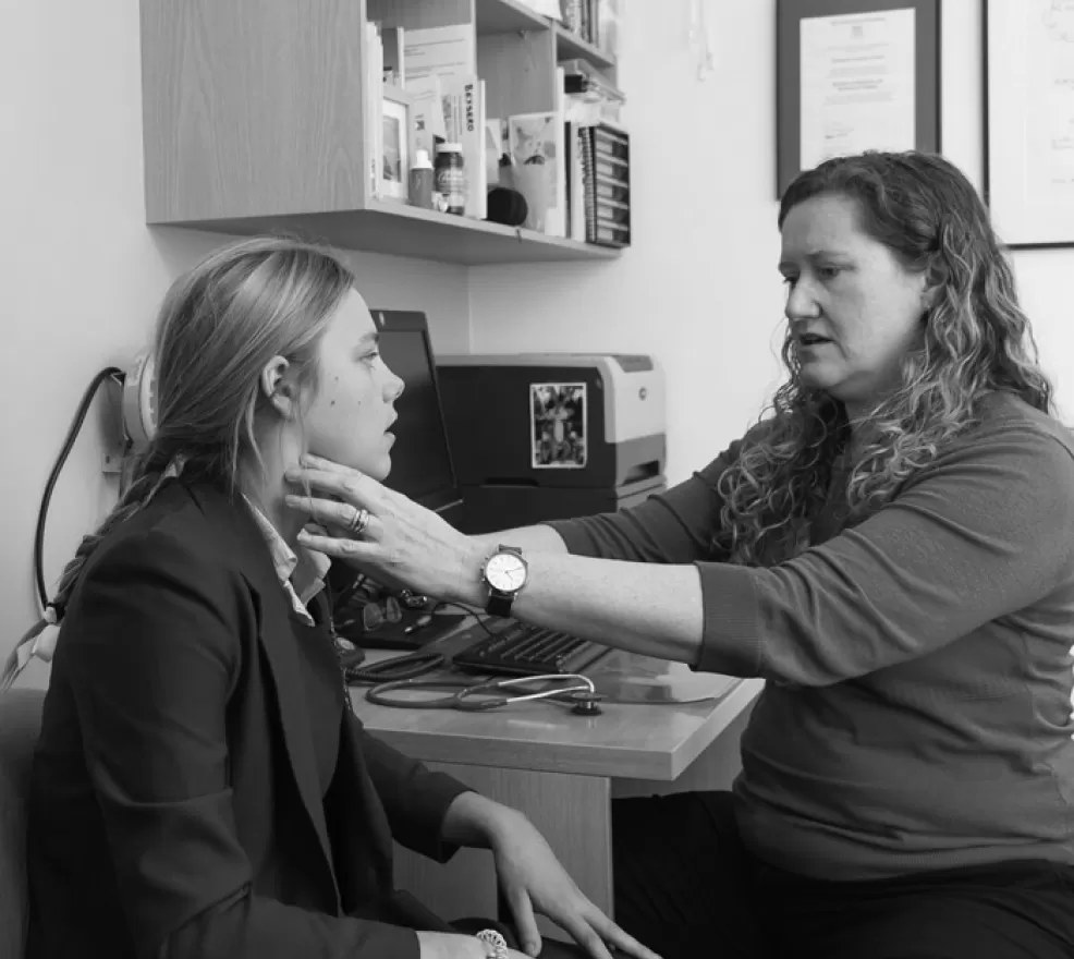 A doctor examining a patient's neck and thyroid during a consultation