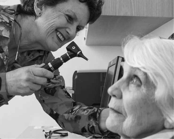 A doctor examining an older patient's ear with an otoscope