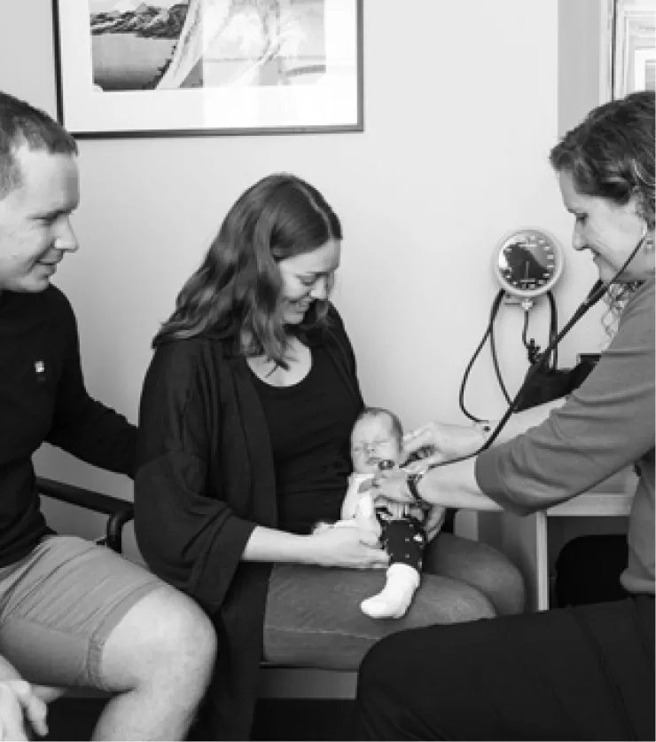 A doctor checking a baby held by a parent while the other parent looks on