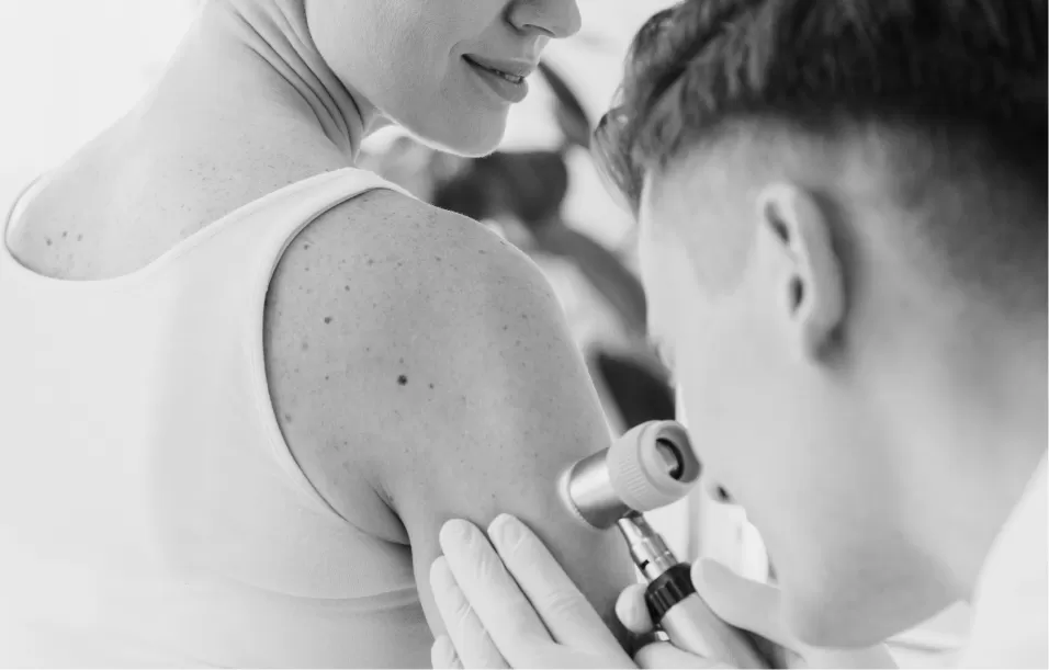 A doctor examining moles on a patient's shoulder with a dermatoscope