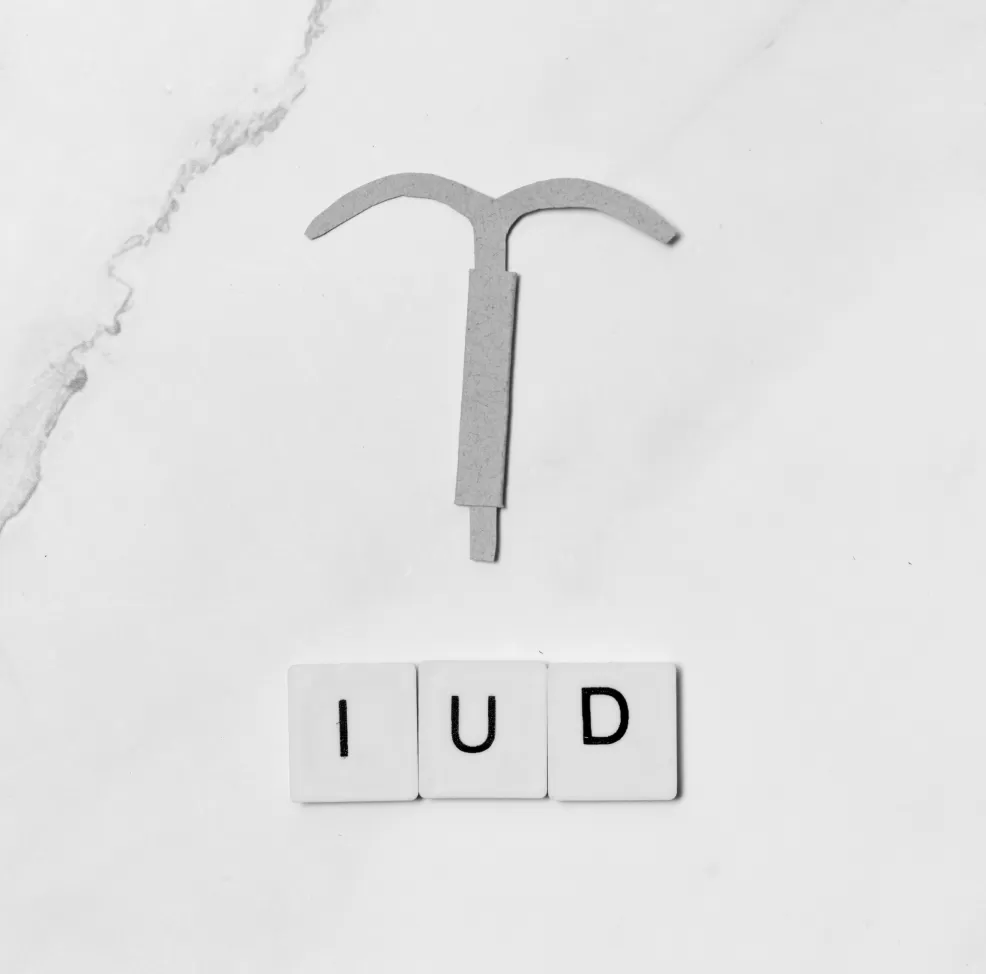 A T-shaped intrauterine device beside letter tiles spelling IUD