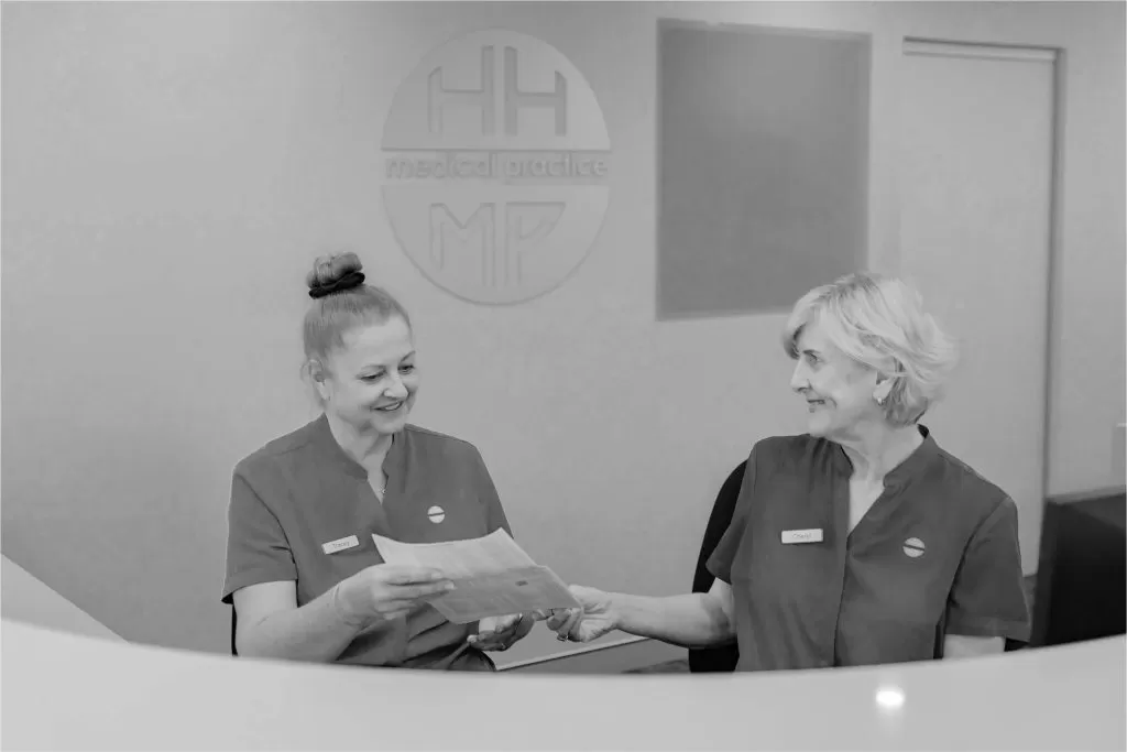 Two reception staff talking over paperwork at the front desk