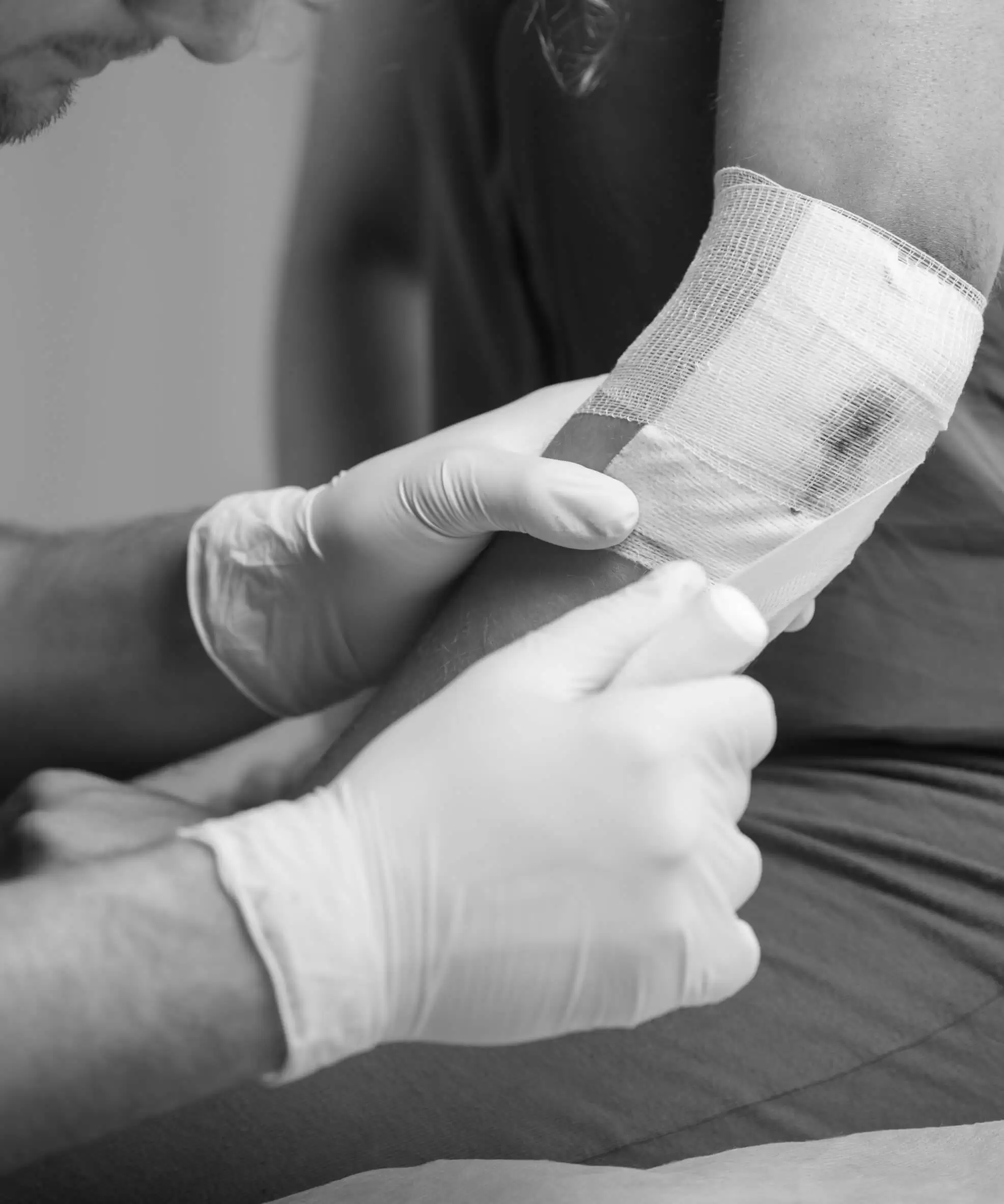 A gloved clinician applying a bandage to a patient's arm