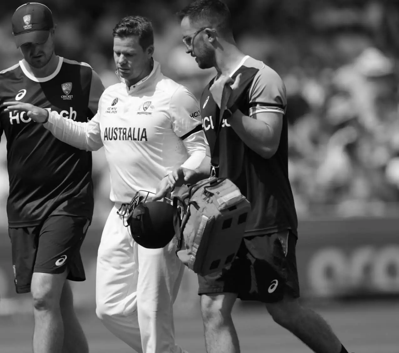 An injured cricketer being helped from the field by medical staff