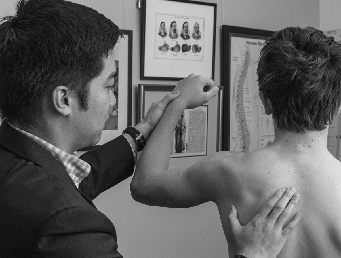 A physiotherapist examining a patient's shoulder beside an anatomy chart